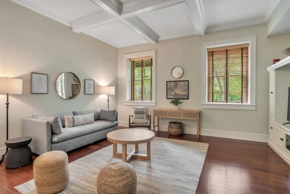 A spacious, light-filled living area highlighted by a comfortable sofa, coffee table, decorative wall art, and large windows that stream in the morning sun. The space is arranged for socializing, entertaining, or unwinding together after a day out in Asheville.