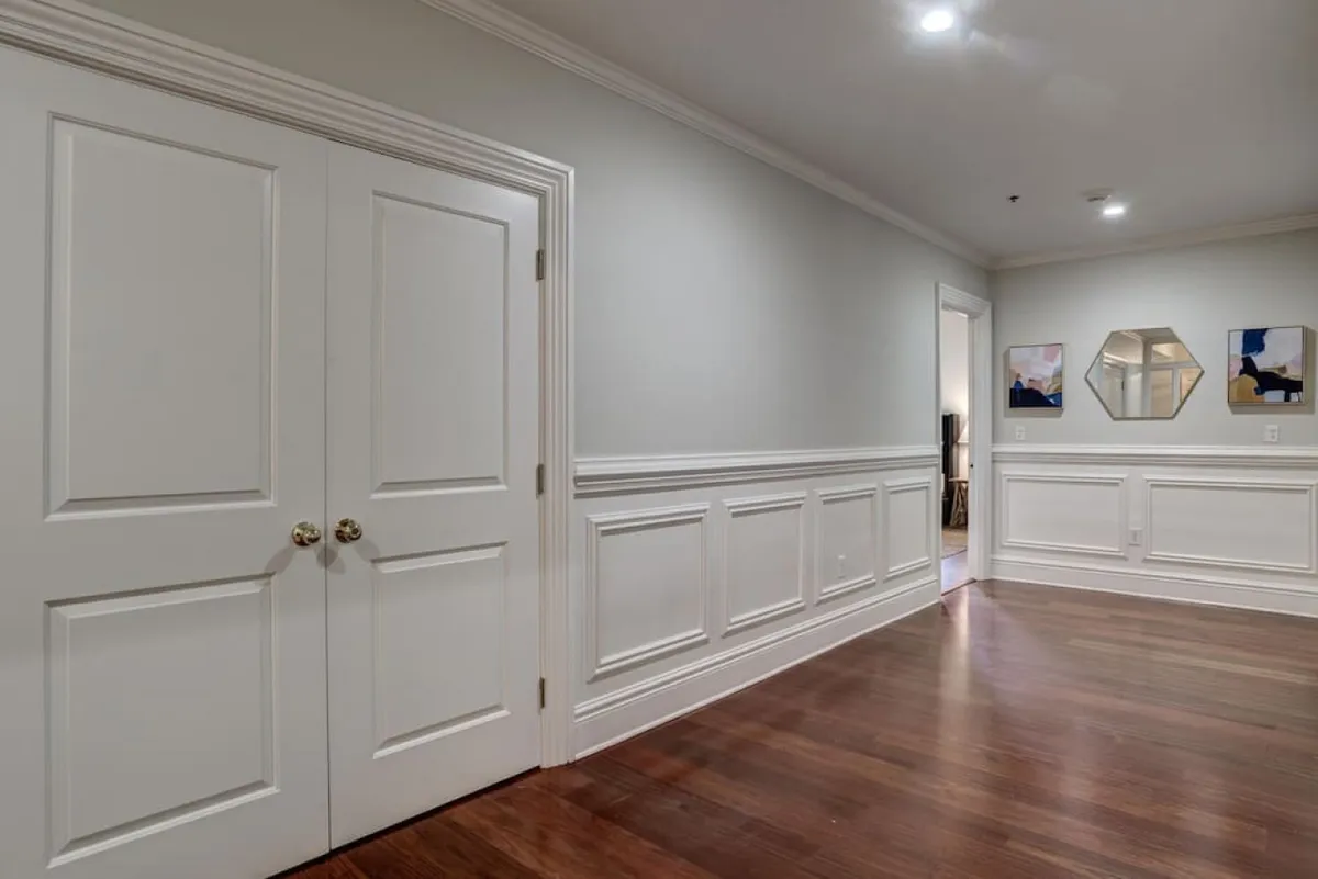 A view through double doors reveals decorative wall paneling and curated artwork adorning the walls, offering a sense of anticipation and highlighting the home’s unique character.