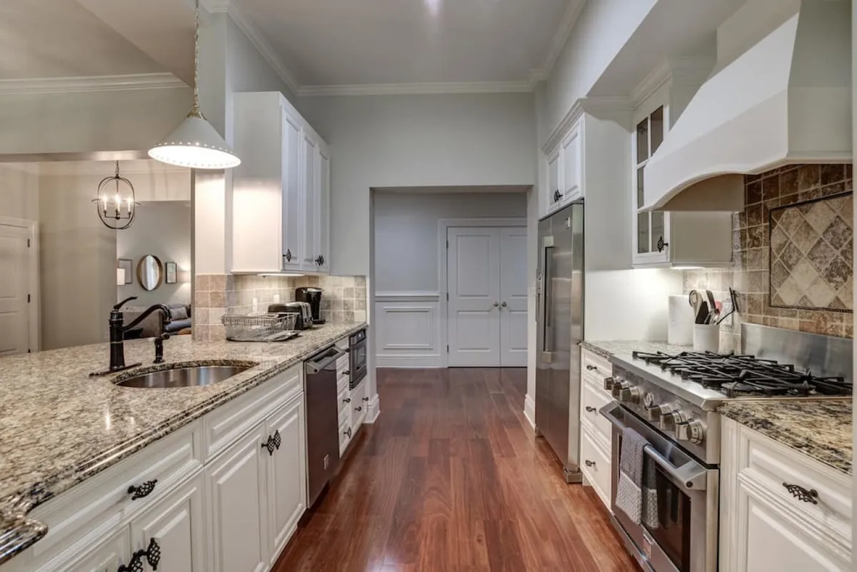 This image presents another angle of the kitchen, emphasizing the granite countertop, sleek stainless steel appliances, crisp white cabinetry, and stylish pendant lighting. The open format creates a functional and aesthetically appealing culinary space.